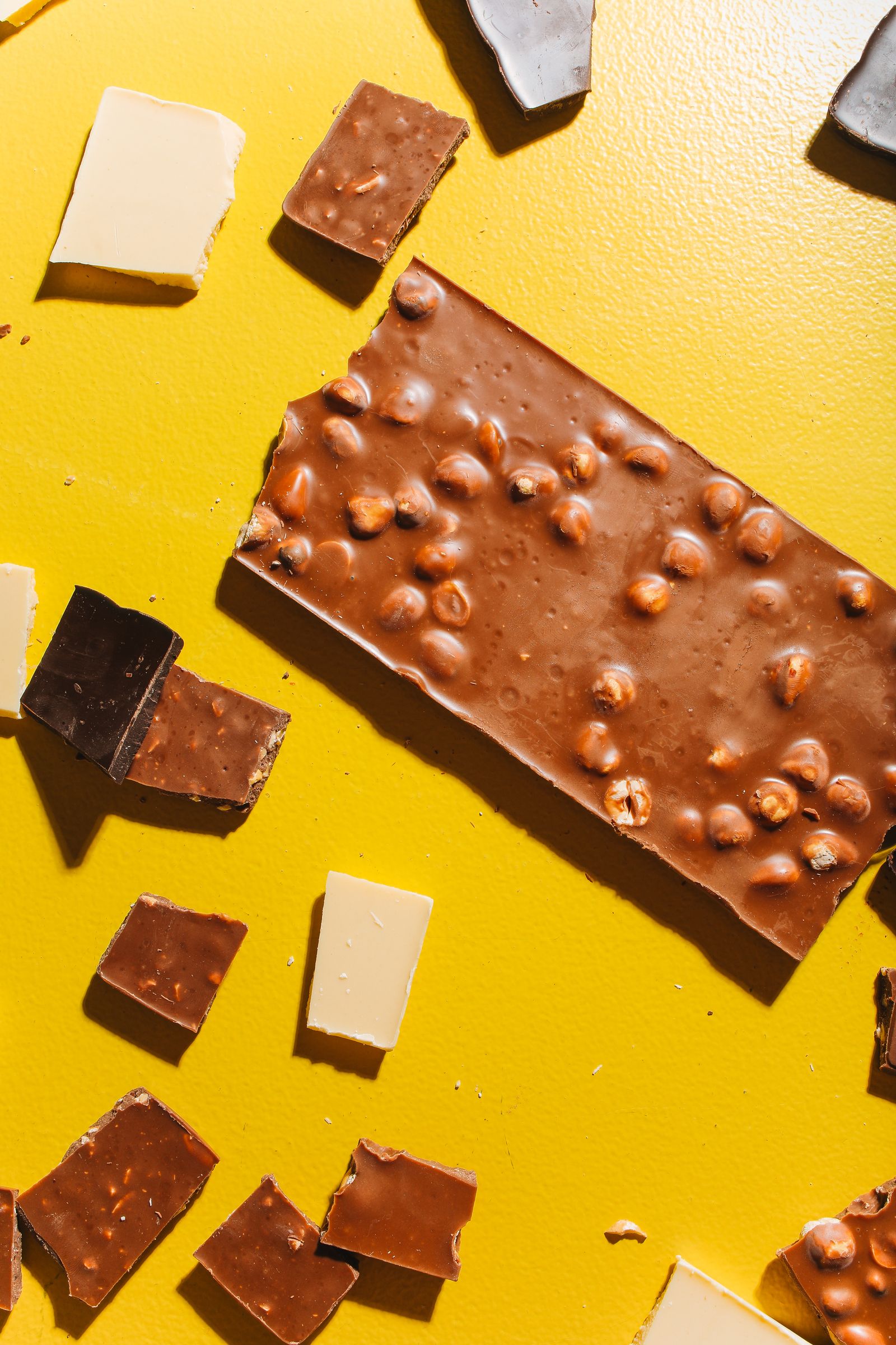 Chunky hazelnut chocolate bar and broken pieces on a bright yellow background